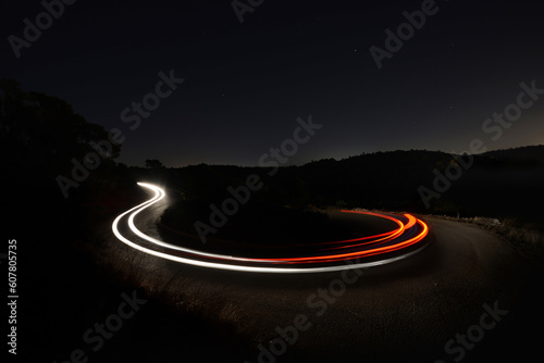 Fototapeta Naklejka Na Ścianę i Meble -  A photo of a car's light trails on a curvy turn during the night with a dark background 