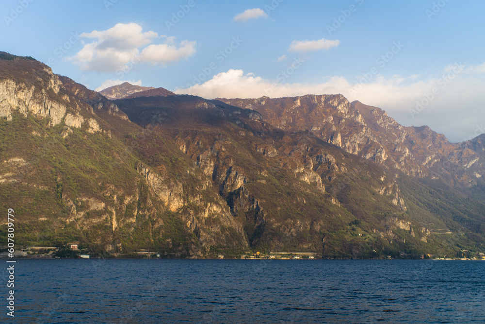 Lake Como from the shore of the town of Bellagio. View of the Alps mountains, buildings and a passenger ferry. Sunset