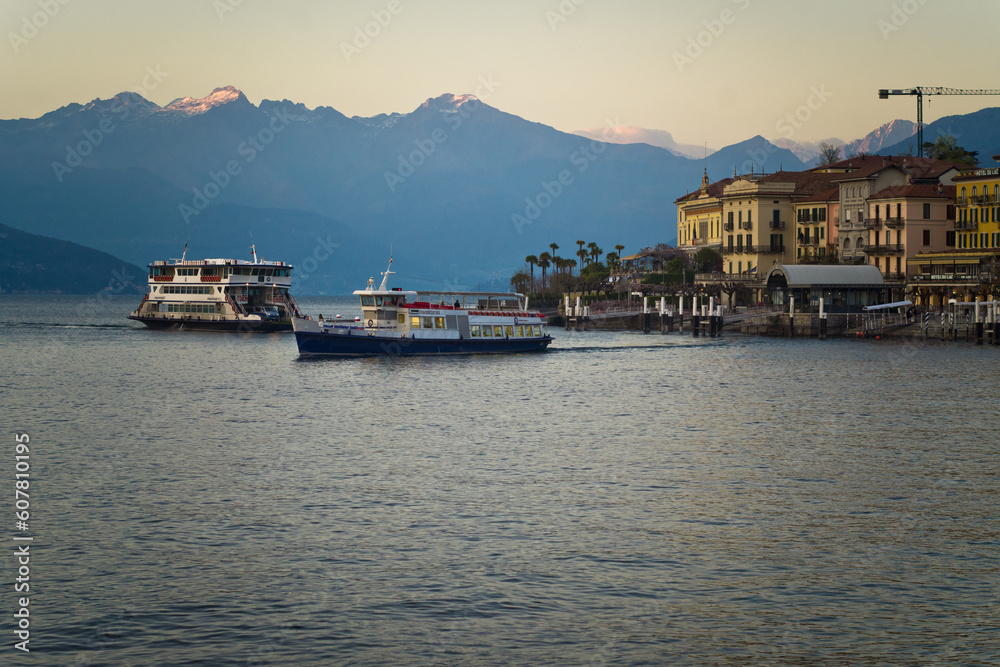 Lake Como from the shore of the town of Bellagio. View of the Alps mountains, buildings and a passenger ferry. Sunset