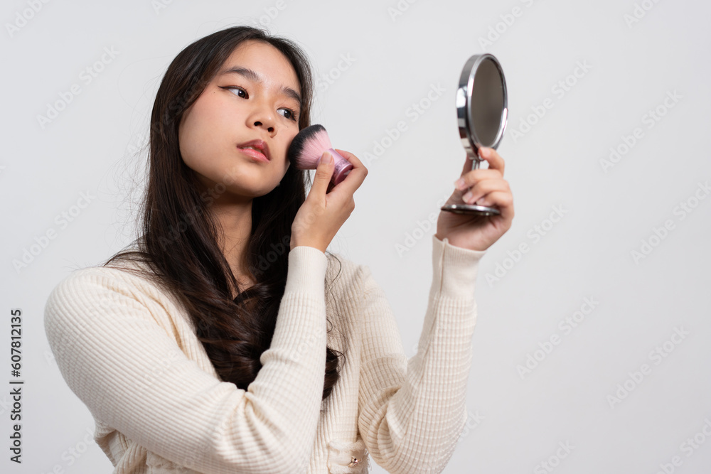 Beautiful young woman makes blush on her face using makeup brush on isolated white background. Teenage girl doing her own makeup. Close up portrait. Copy, empty space for text Beautiful young woman makes blush on her face using makeup brush on isolated white background. Teenage girl doing her own makeup. Close up portrait. Copy, empty space for text