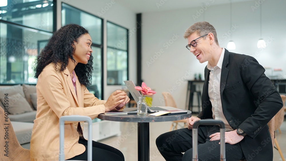 Two businesspeople brainstorm working together using laptop sitting in airline lounge with luggage while waiting flight. Business trip concept