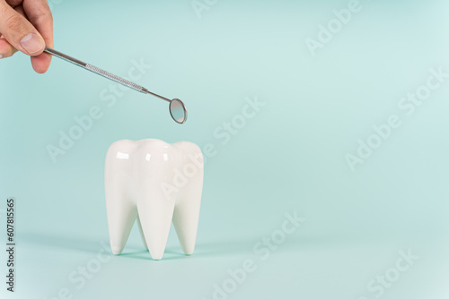 Dental treatment concept. Dental offers free treatment. Healthy white tooth model and dental mirror on a blue background with copy space. Teeth care, whitening, tooth extraction, implant concept. © Dina Photo Stories