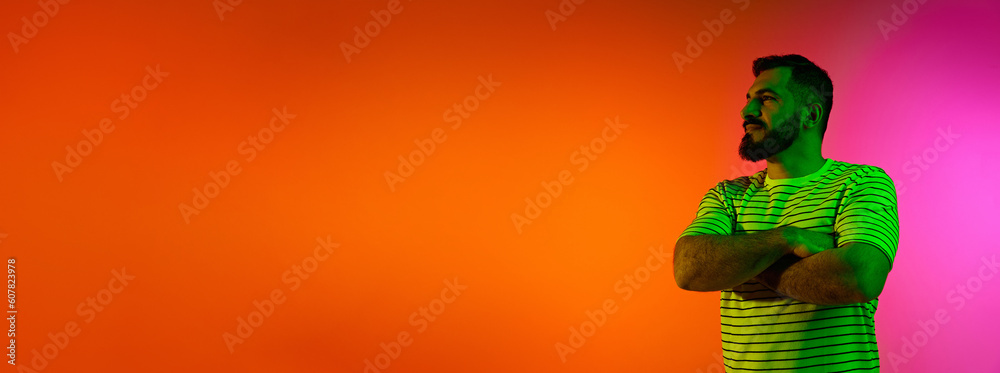 Bearded handsome man standing with serious and confident face against gradient studio background in neon light. Concept of human emotions, facial expression, lifestyle. Banner. Copyy space for ad Bearded handsome man standing with serious and confident face against gradient studio background in neon light. Concept of human emotions, facial expression, lifestyle. Banner. Copyy space for ad
