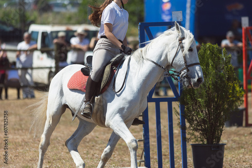 A girl in white uniform riding white horse at the ranch