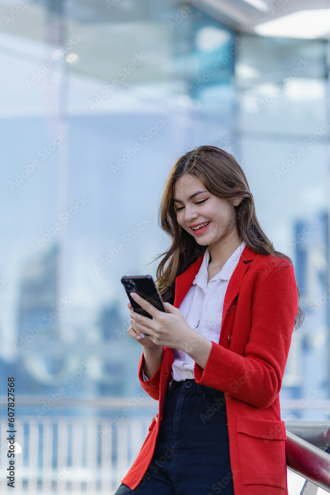 Attractive woman happily standing and discussing work on the phone near her office building. Smiling woman holding smartphone talking to customer walking on outdoor street