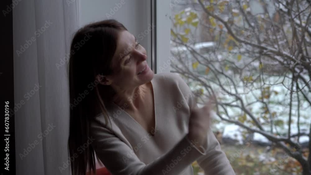 Zoom in portrait of joyful young woman sitting on windowsill waving looking out window talking smiling. Happy positive Caucasian lady inviting neighbors