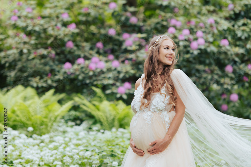 A beautiful pregnant woman wearing a luxurious dress is standing in a blooming rhododendron garden A beautiful pregnant woman wearing a luxurious dress is standing in a blooming rhododendron garden