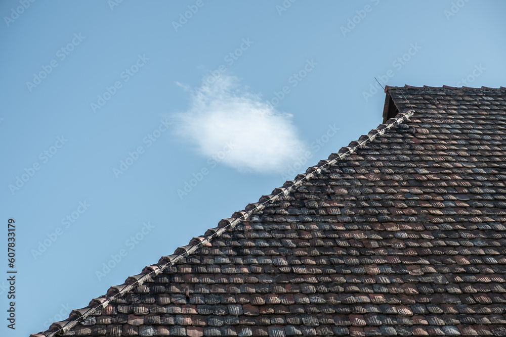 Detail Walmdach mit historischen Dachziegeln vor blauem Himmel mit weisser Wolke Detail Walmdach mit historischen Dachziegeln vor blauem Himmel mit weisser Wolke