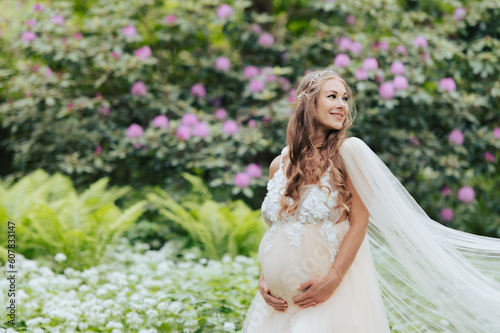 A beautiful pregnant woman wearing a luxurious dress is standing in a blooming rhododendron garden