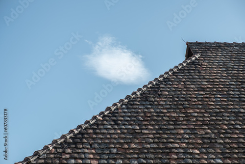 Detail Walmdach mit historischen Dachziegeln vor blauem Himmel mit weisser Wolke © lebaer