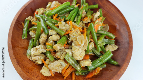 Tumis buncis, wortel and tempe or stir-fry beans, carrots and tempeh. Served on a wooden plate and isolated on a white background. photo