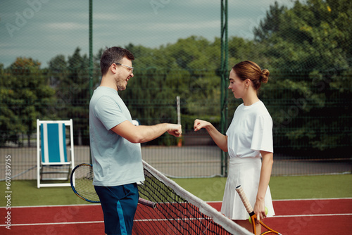 Young man and girl giving fist bump with fist before playing tennis. Fit athlete couple standing and using hand gesture for good luck.
