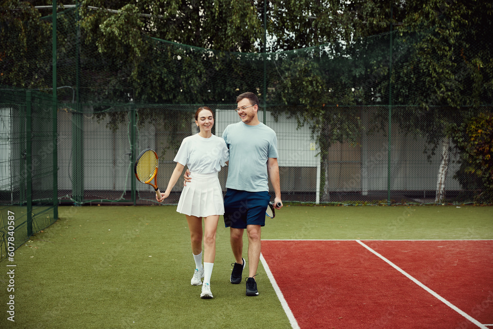 Young couple on tennis court. Two tennis players are smiling and walking around the court and talking