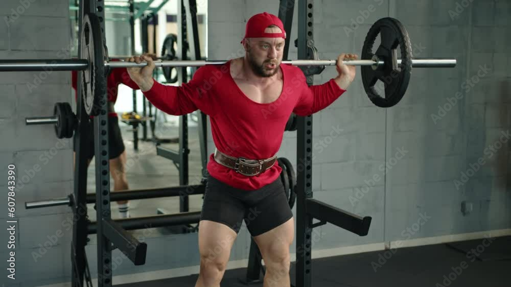 professional bodybuilder squats with a barbell in the gym, dressed in red clothes.slow motion professional bodybuilder squats with a barbell in the gym, dressed in red clothes.slow motion