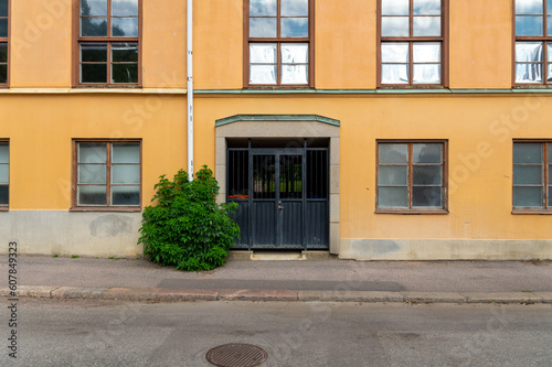 A Black metal gate to a yellow building with a bush next to it.