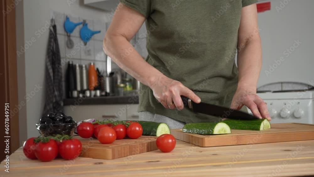 Woman cutting fresh cucumber for greek salad at home kitchen Woman cutting fresh cucumber for greek salad at home kitchen