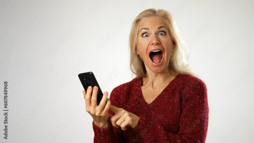 Fototapeta premium Happy middle aged woman holding smartphone, using mobile applications pointing to phone isolated on white background.