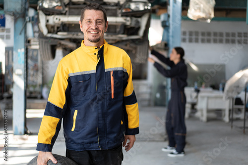 Caucasian man mechanic holding car tire with car lift background at car service 