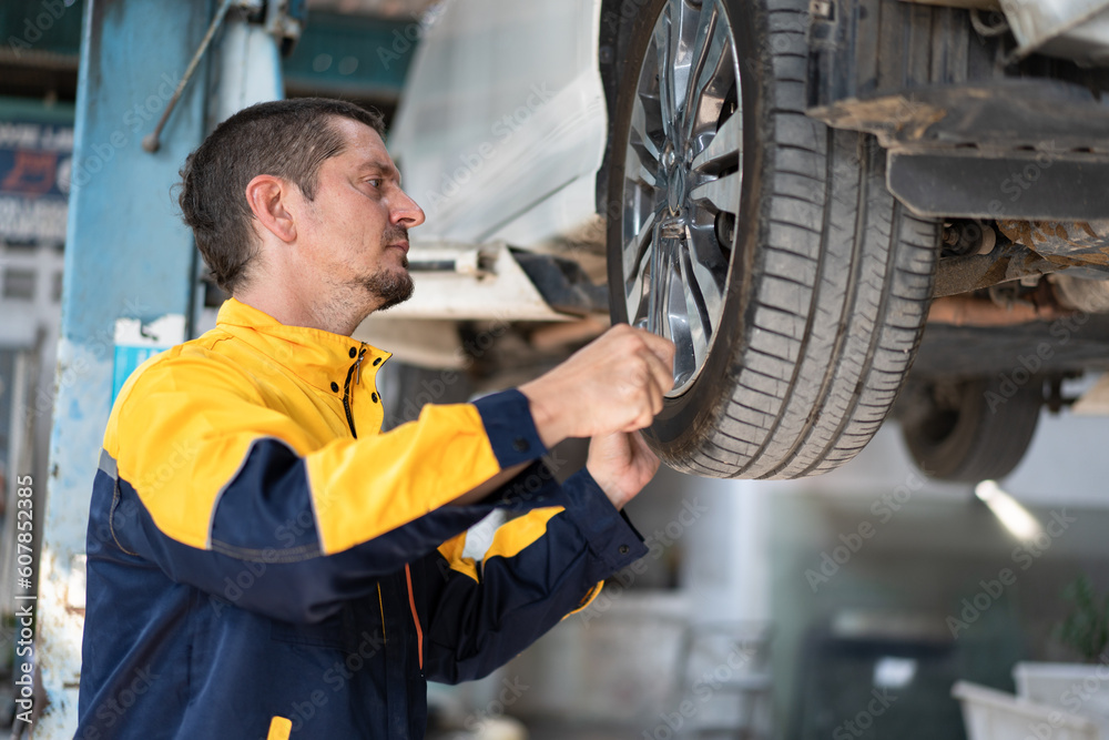 Caucasian man mechanic checking and repair car tire on car lift at car service Caucasian man mechanic checking and repair car tire on car lift at car service