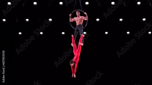 Circus aerial hoop duo on black background performing beautiful tricks. Man and women fly on stage