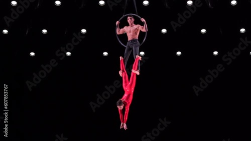 Circus aerial hoop duo with on black stage background performing trick, highly risky drop. Concept of trust and confidence