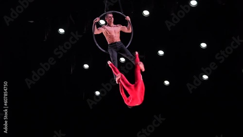 Circus aerial hoop duo on black background performing risky tricks. Man and women fly on stage