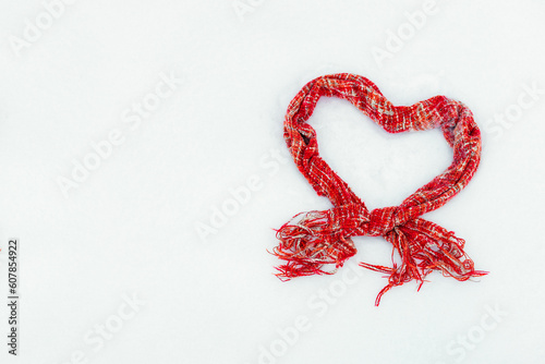red knitted scarf in the shape of a heart on white snow in winter, free space