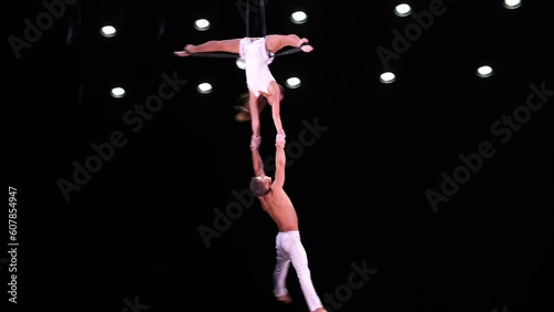 Aerial straps duo with white costume on black stage background performing and flying high
