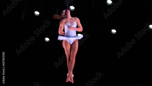 Female circus artist on Aerial straps on black background performing spinning trick on the neck. Concept of individuality, creativity and self-confidence