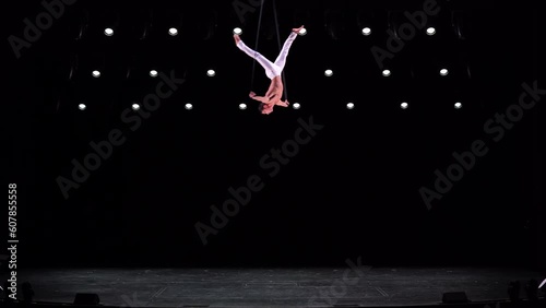 Male, muscular circus artist on Aerial straps on black stage background performing gymnastics trick