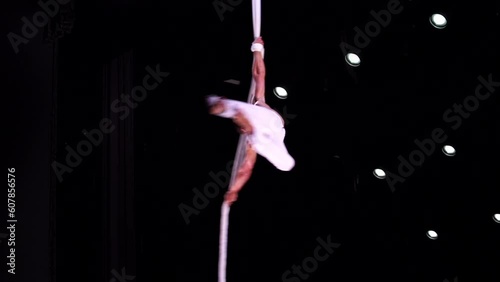 Male, muscular circus artist on Aerial straps on black stage background performing spinning trick in slow motion