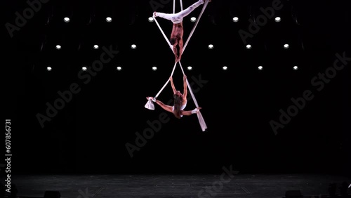 Aerial silk duo in white costumes on black background performing. Concept of desire, attraction and relationship