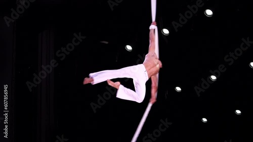 Male, muscular circus artist on Aerial silk on black stage background performing spinning trick. Concept of individuality, creativity and self-confidence