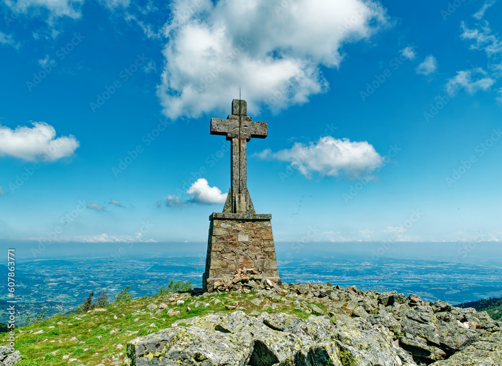 Massive stone cross on top of Cret de l'Oeillon mountain in Pilat, beautiful blue sky with scattered clouds, France