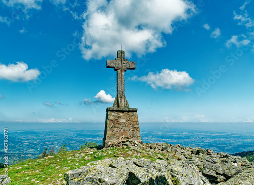 Massive stone cross on top of Cret de l'Oeillon mountain in Pilat, beautiful blue sky with scattered clouds, France