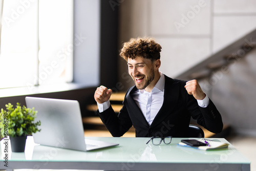 Happy businessman achiving his goal and showing fists at office photo