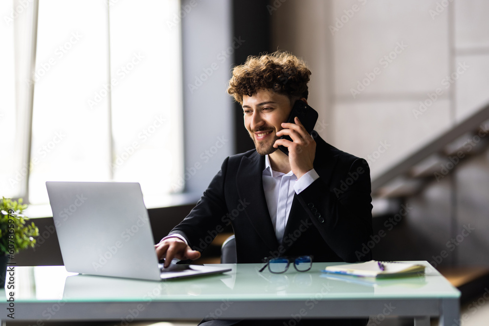 Bearded man at the wooden desk talking on the phone in office Bearded man at the wooden desk talking on the phone in office