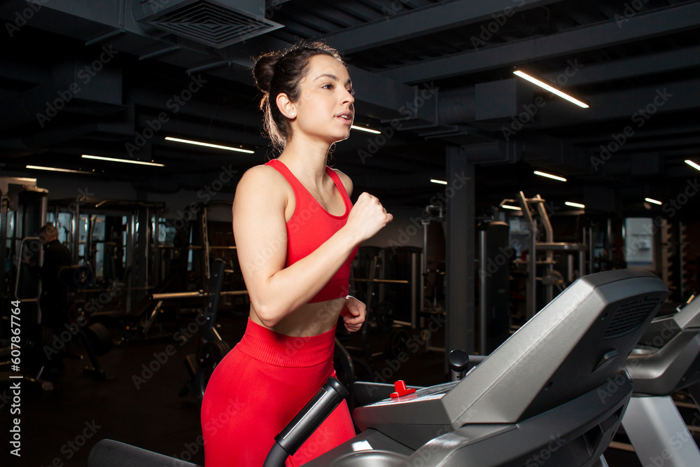 sports girl in red sportswear runs on treadmill in the gym, woman trains in fitness room sports girl in red sportswear runs on treadmill in the gym, woman trains in fitness room