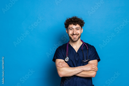 Happy smiling doctor or male nurse in blue uniform with crossed arms over blue background