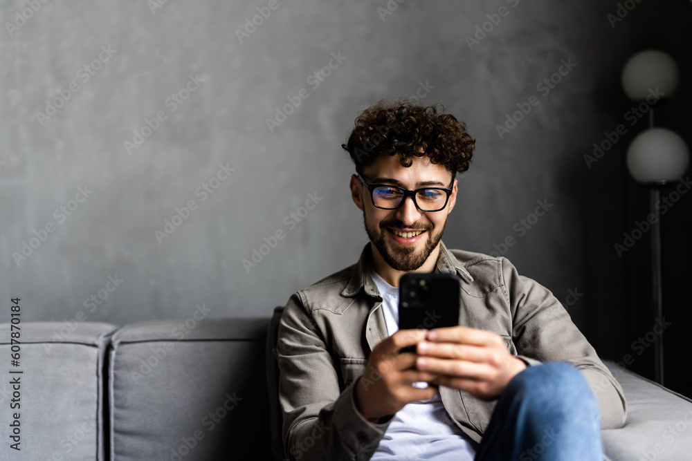 Content young man relax on sofa use smartphone spend free time online in social network chat at web app play easy game online. Content young man relax on sofa use smartphone spend free time online in social network chat at web app play easy game online.