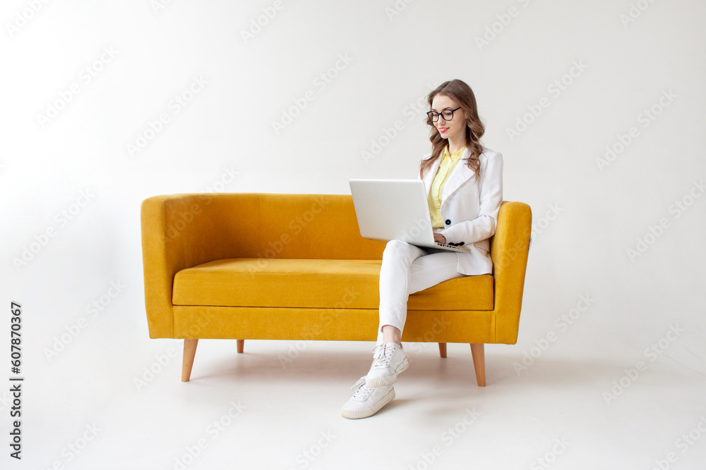 young businesswoman in suit sits on comfortable soft sofa and uses laptop, girl in formal wear is typing on computer young businesswoman in suit sits on comfortable soft sofa and uses laptop, girl in formal wear is typing on computer