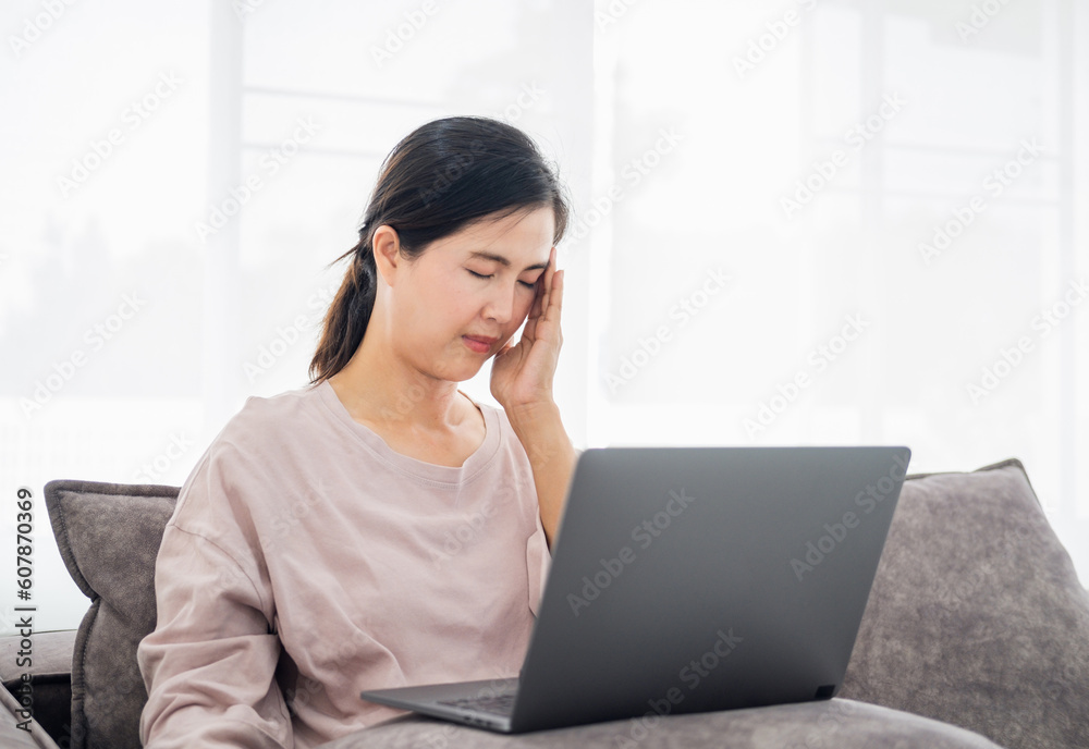 Asian mature woman wearing glasses seriously working on computer laptop sitting on sofa couch in living room house. She thinking find solution problem of work. Asian mature woman wearing glasses seriously working on computer laptop sitting on sofa couch in living room house. She thinking find solution problem of work.
