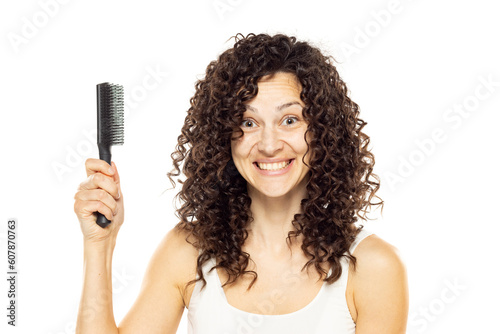Portrait shot of beautiful young woman model with curly dark hair looking at camera with charming cute smile while holding a hair brush against white background