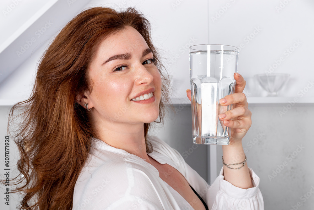 A beautiful healthy brunette girl is holding a glass of water or clear liquid, smiling happy positive. demonstrating product vitamins, hydrating drinks, alcohol. A beautiful healthy brunette girl is holding a glass of water or clear liquid, smiling happy positive. demonstrating product vitamins, hydrating drinks, alcohol.