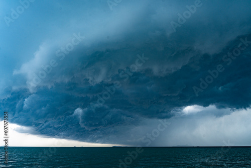 View of tropical ocean storm with menacing clouds and rain showering below, Light in the dark and dramatic storm clouds background © chokniti