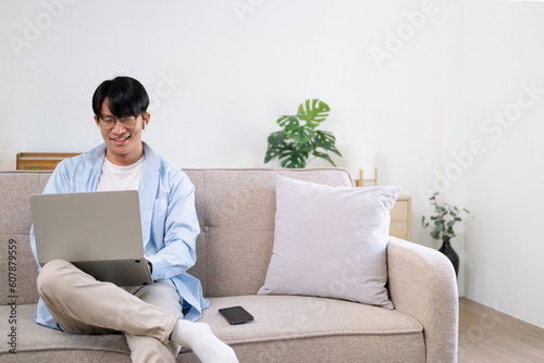 Happy satisfied millennial man using laptop at living room, working from home, reading message with good news, thinking, looking at screen, watching online webinar, training, making payment