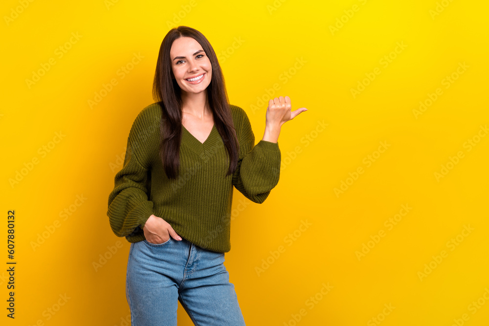 Photo of pretty positive person indicate thumb finger empty space ad isolated on yellow color background Photo of pretty positive person indicate thumb finger empty space ad isolated on yellow color background