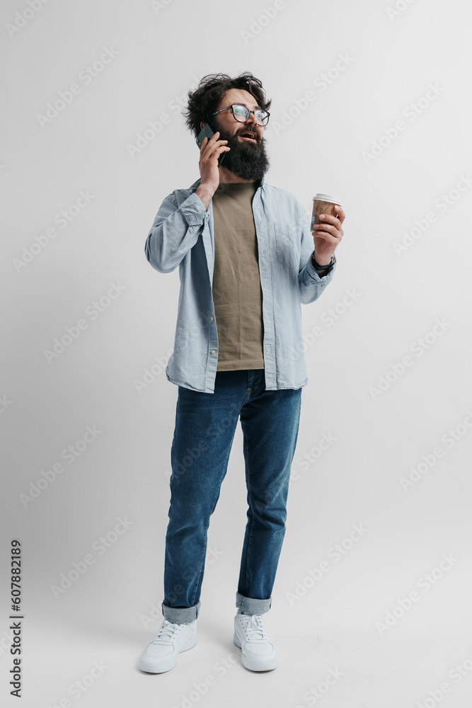 Full length body portrait of a handsome hipster man wearing stylish clothes drinking coffee and and talking on smartphone on a white background Full length body portrait of a handsome hipster man wearing stylish clothes drinking coffee and and talking on smartphone on a white background