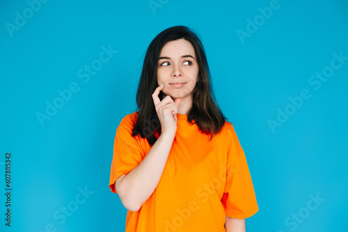 Attractive Young Woman in Trendy Orange Clothes, Pensive and Skeptical Expression, Empty Space for Copy, Isolated on Blue Background - Portrait Photo
