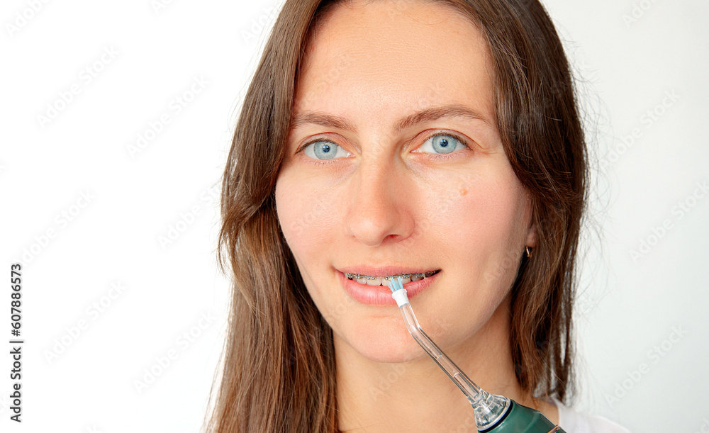 portrait of a young woman with braces brushing her teeth with an irrigator. Blue eyes, plain clothes, brown hair. water flosser portrait of a young woman with braces brushing her teeth with an irrigator. Blue eyes, plain clothes, brown hair. water flosser